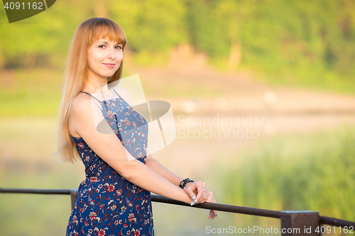 Image of The charming young girl standing on a rustic bridge at dawn sun