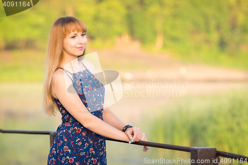 Image of The charming young girl standing on a rustic bridge over the river at dawn sun
