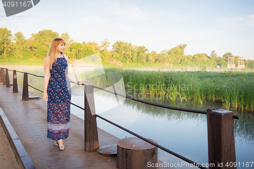 Image of The charming young girl walking on the bridge over the river at dawn