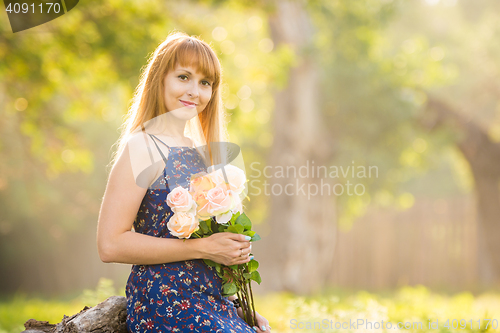 Image of Beautiful young woman looking with a bouquet of roses in hands on a background of green sunny blurred