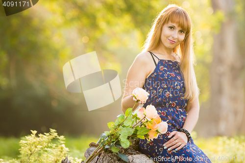 Image of Beautiful young girl on the background of the sunny blurred greenery, lies next to a bouquet of roses