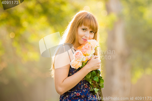 Image of Beautiful young sexy girl standing with a bouquet of roses on a background of green sunny blurred