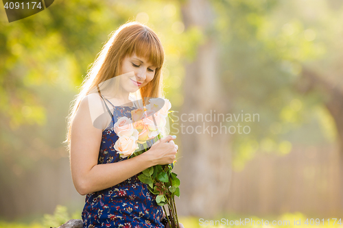 Image of Beautiful young sexy girl looks at a bouquet of roses given to her standing against a background of green sunny blurred