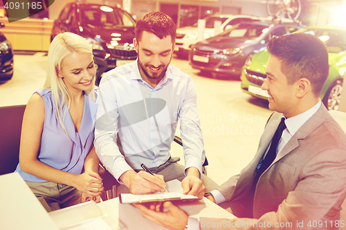 Image of happy couple with car dealer in auto show or salon