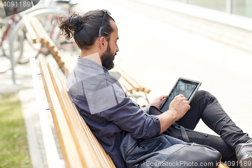 Image of man with tablet pc sitting on city street bench