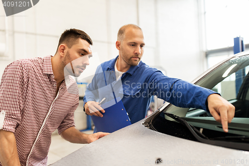 Image of auto mechanic with clipboard and man at car shop