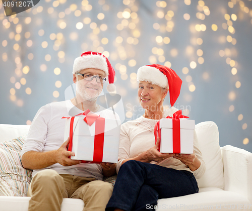 Image of happy senior couple in santa hats with gift boxes