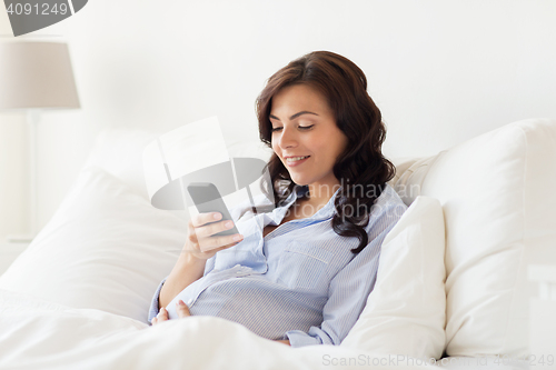 Image of happy pregnant woman with smartphone in home bed