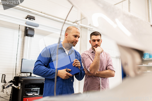 Image of auto mechanic with clipboard and man at car shop