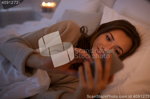 Image of young woman with smartphone in bed at home bedroom