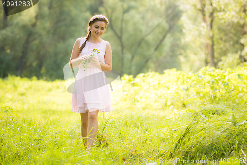 Image of Young girl in the summer light dress collecting wild flowers