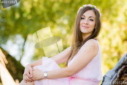 Image of Beautiful girl sits on a background illuminated by the sun leaves