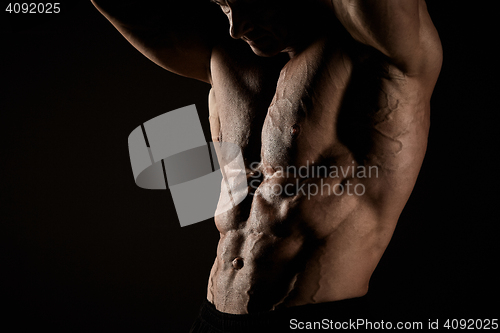 Image of torso of attractive male body builder on black background.