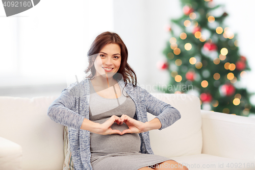 Image of happy pregnant woman making heart gesture at home