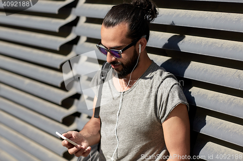 Image of man with earphones and smartphone on city street