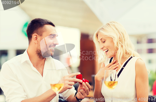 Image of happy couple with engagement ring and wine at cafe