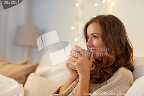 Image of happy woman with cup of coffee in bed at home