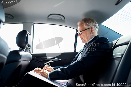 Image of senior businessman with papers driving in car