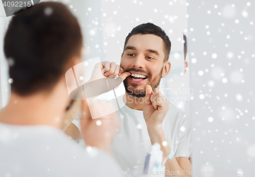 Image of man with dental floss cleaning teeth at bathroom