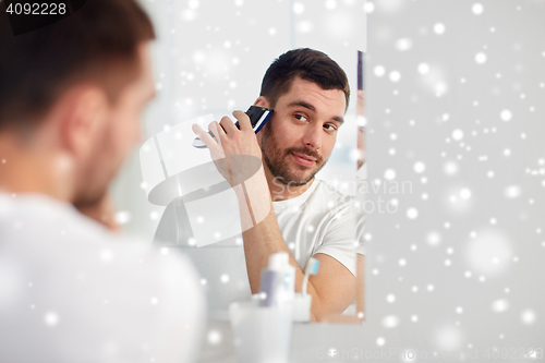 Image of man shaving beard with trimmer at bathroom