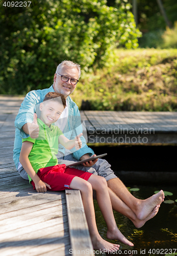 Image of grandfather and boy with tablet pc on river berth