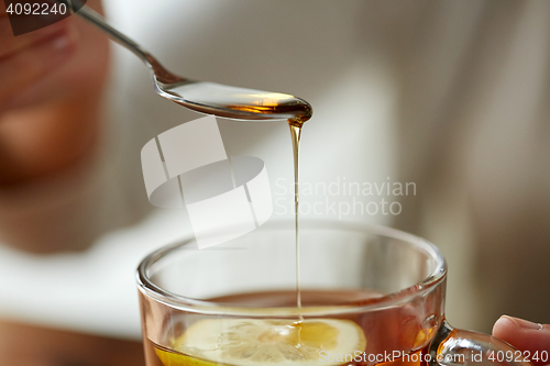 Image of close up of woman adding honey to tea with lemon