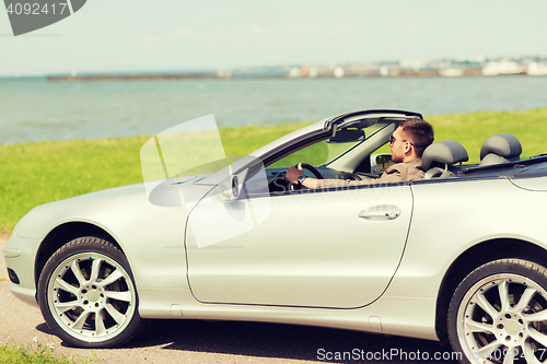 Image of happy man driving cabriolet car outdoors