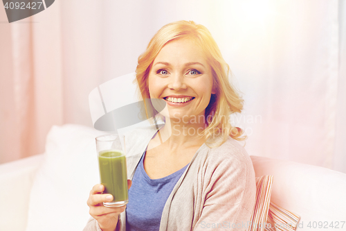 Image of happy woman drinking green juice or shake at home