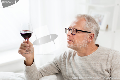 Image of senior man drinking red wine from glass at home