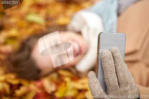 Image of woman on autumn leaves taking selfie by smartphone