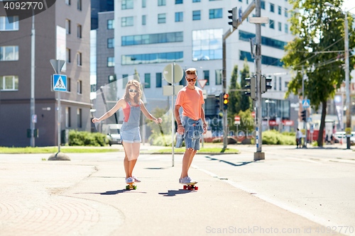 Image of teenage couple riding skateboards on city street