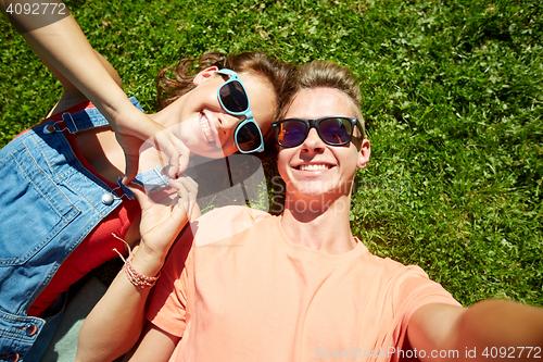 Image of happy teenage couple taking selfie on summer grass