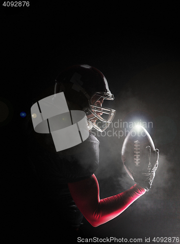 Image of American football player posing with ball on black background