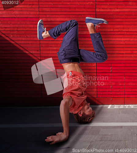 Image of Break dancer doing handstand against red wall background