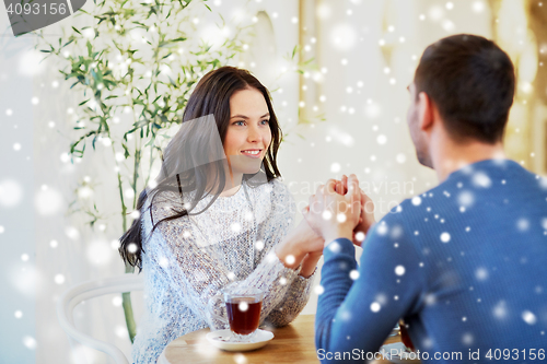 Image of happy couple with tea holding hands at restaurant