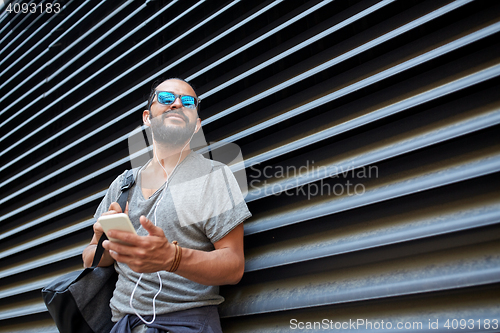 Image of man with earphones and smartphone on city street
