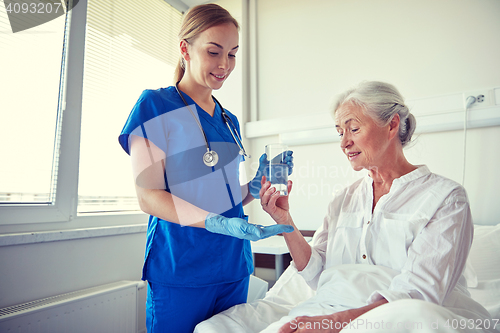 Image of nurse giving medicine to senior woman at hospital