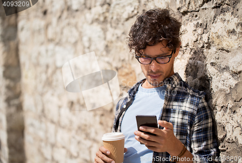 Image of man with smartphone drinking coffee on city street