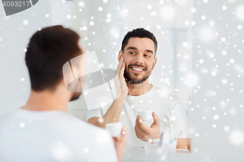 Image of happy young man applying cream to face at bathroom