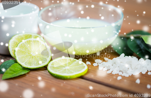 Image of body lotion in bowl and limes on wood