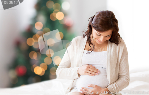 Image of happy pregnant woman sitting on bed at christmas