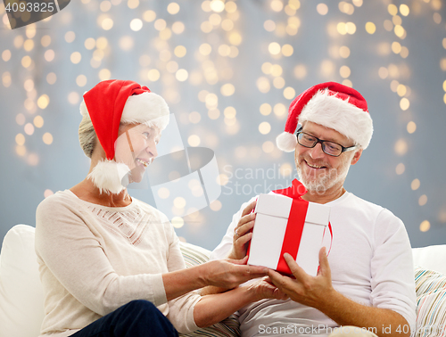 Image of happy senior couple in santa hats with gift box