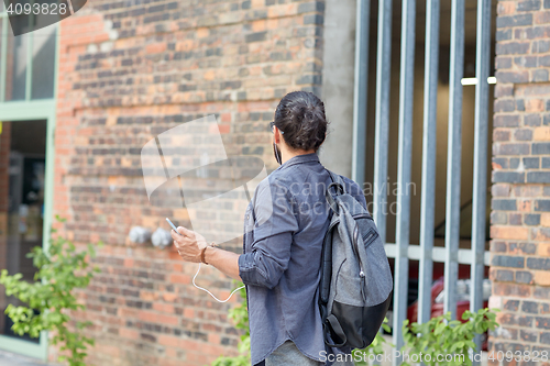 Image of man with backpack and smartphone walking in city