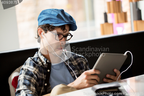 Image of man with tablet pc and earphones sitting at cafe