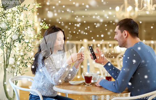 Image of happy couple with smartphones drinking tea at cafe