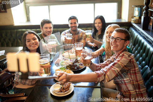 Image of happy friends with selfie stick at bar or pub