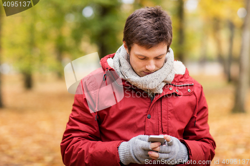 Image of young man with smartphone walking at autumn park