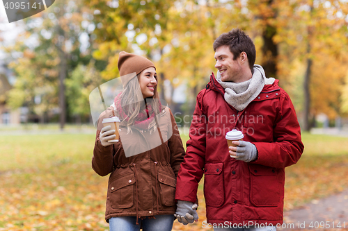 Image of happy couple with coffee walking in autumn park