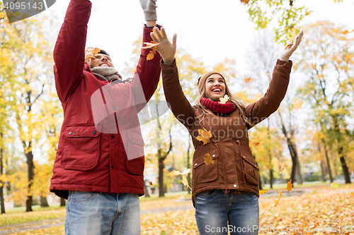 Image of happy young couple throwing autumn leaves in park