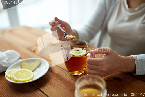 Image of close up of woman adding honey to tea with lemon